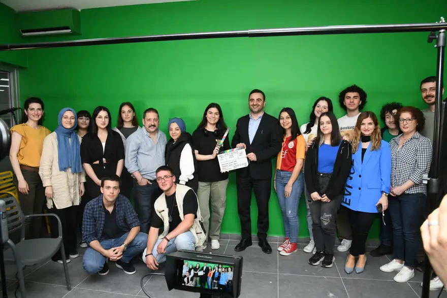 Başkan Özlü, yeşil perde önünde klaket tutan gençlerle poz veriyor