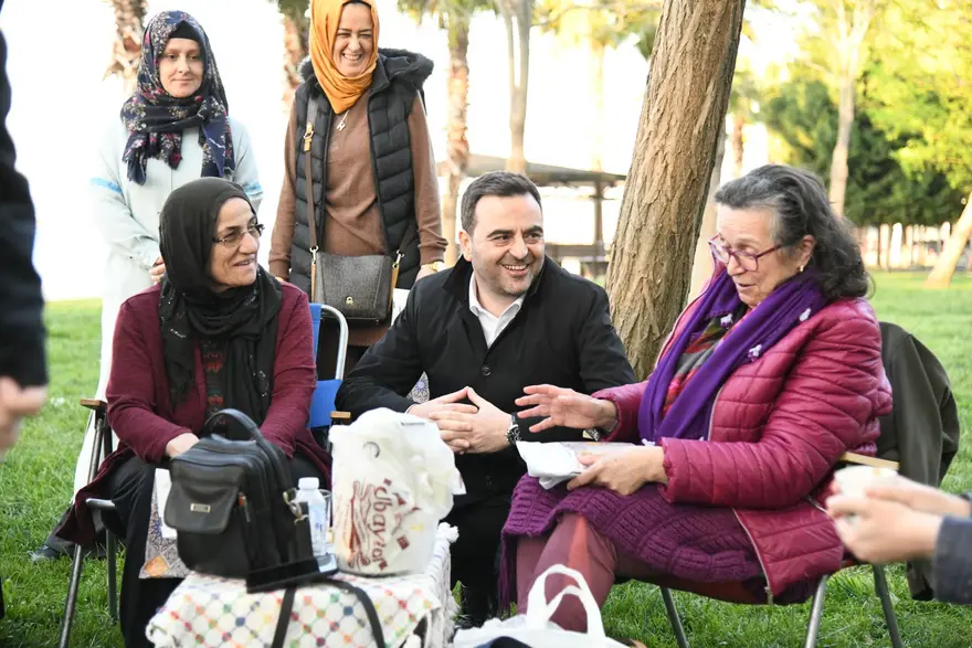 Bankta oturan kadınlar ve Başkan Özlü birlikte gülüyor